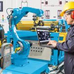 Engineer_using_laptop_computer_for_control_automatic_robotic_hand_machine_tool_at_industrial_manufacture_factory