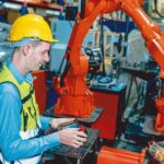 Worker_man_working_with_robot_arm_automate_welding_machine_in_modern_metal_factory._Engineer_program_robotic_in_heavy_industry.
