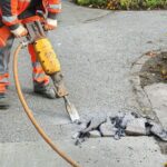 Worker_at_construction_site_demolishing_asphalt_with_pneumatic_plugger_hammer