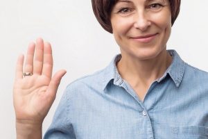 Positive_mature_caucasian_woman_smiling_friendly_and_waving_hand_at_camera._Business_and_welcome_concept.