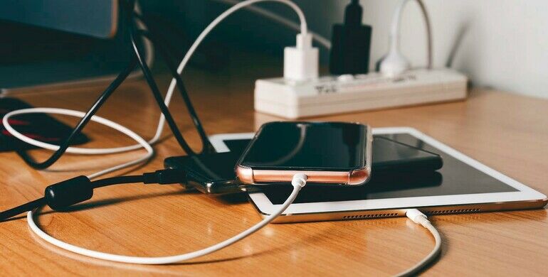 Smart_phone_electronic_gadget_charge_energy_battery_by_adapter_plug._On_wooden_table_in_work_room.