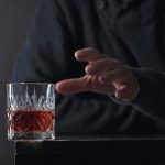 Man's_hand_reaches_for_a_glass_of_alcohol._Conceptual_image_on_the_subject_of_alcoholism._Copy_space_for_your_text.