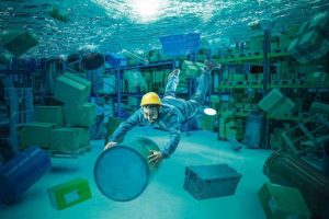 Worker_clings_to_a_bin_in_a_totally_flooded_warehouse._Abstract_underwater_image,_concept_of_problems_at_work.
