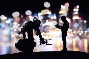 Industry_4.0_technology_,_artificial_intelligence_trend_concept._Silhouette_of_engineer_man_control_to_heavy_automation_robot_arm_machine._Bokeh_flare_light_effect_with_building_background.
