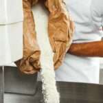 Midsection_of_mid_adult_baker_pouring_flour_in_kneading_machine_at_bakery