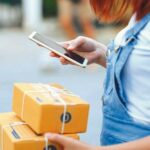 young_woman_hand_holding_smartphone_and_signing_receipt_of_delivery_package,_shipping_and_postal_service_concept