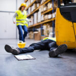 An_accident_in_a_warehouse._Woman_running_towards_her_colleague_lying_on_the_floor_next_to_a_forklift.
